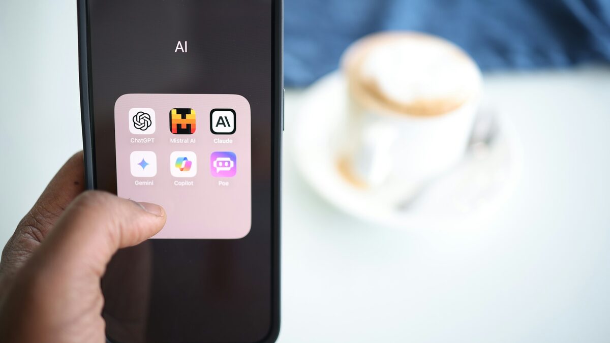 Hand hält ein Smartphone mit einem Ordner voller KI-Apps vor einer Tasse Cappuccino