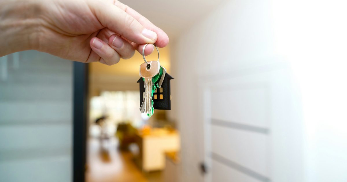 Hand hält einen Schlüsselbund mit hausförmigem Anhänger im Flur einer Wohnung