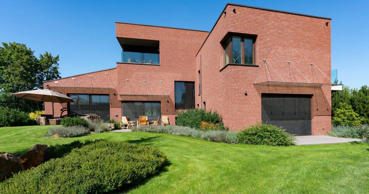 Modernes Einfamilienhaus aus rotem Backstein mit Garten und Terrasse vor blauem Himmel