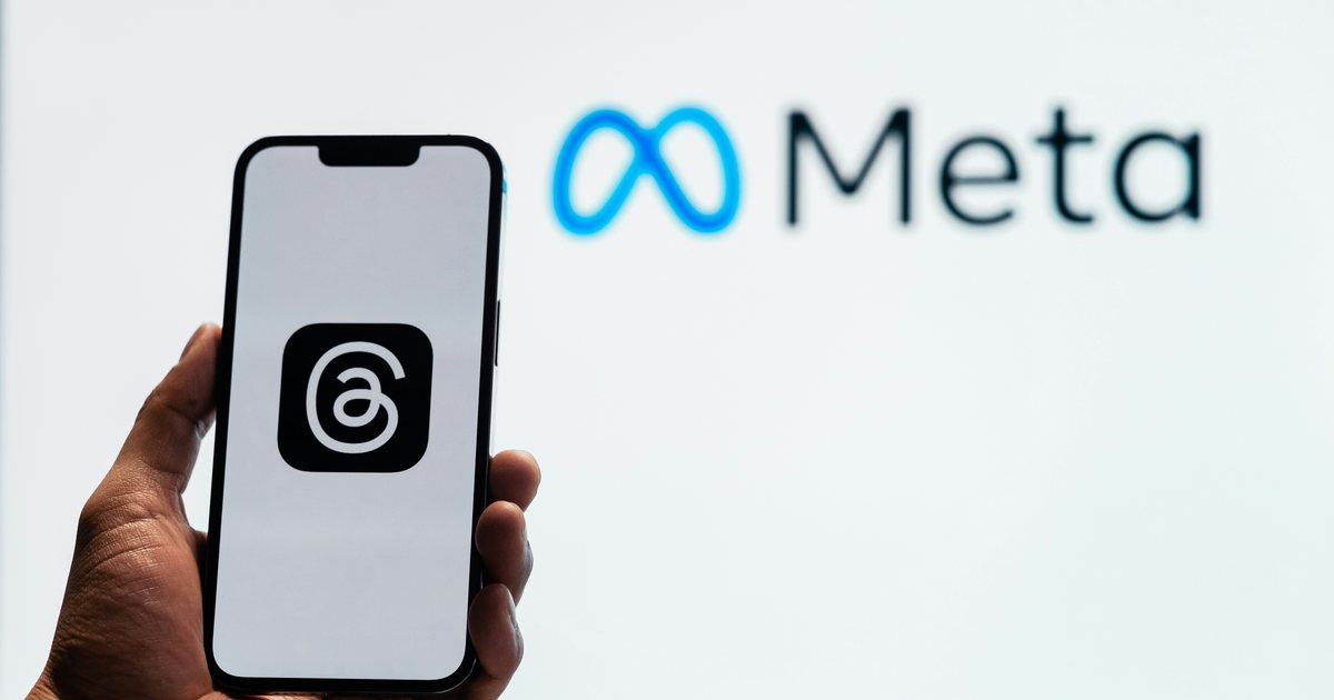 Hand hält ein Smartphone mit dem Threads-Symbol vor einer Wand mit dem Meta-Logo