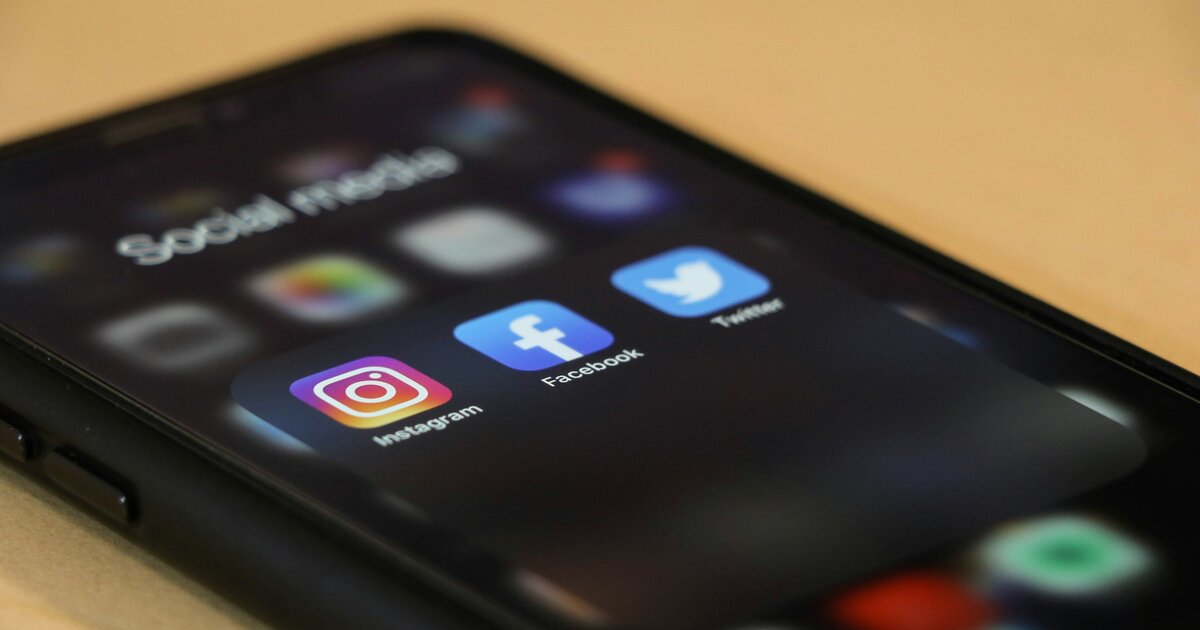 Smartphone auf einem Holztisch, auf dem Bildschirm ein Ordner „Social Media“ mit den Symbolen von Instagram, Facebook und Twitter