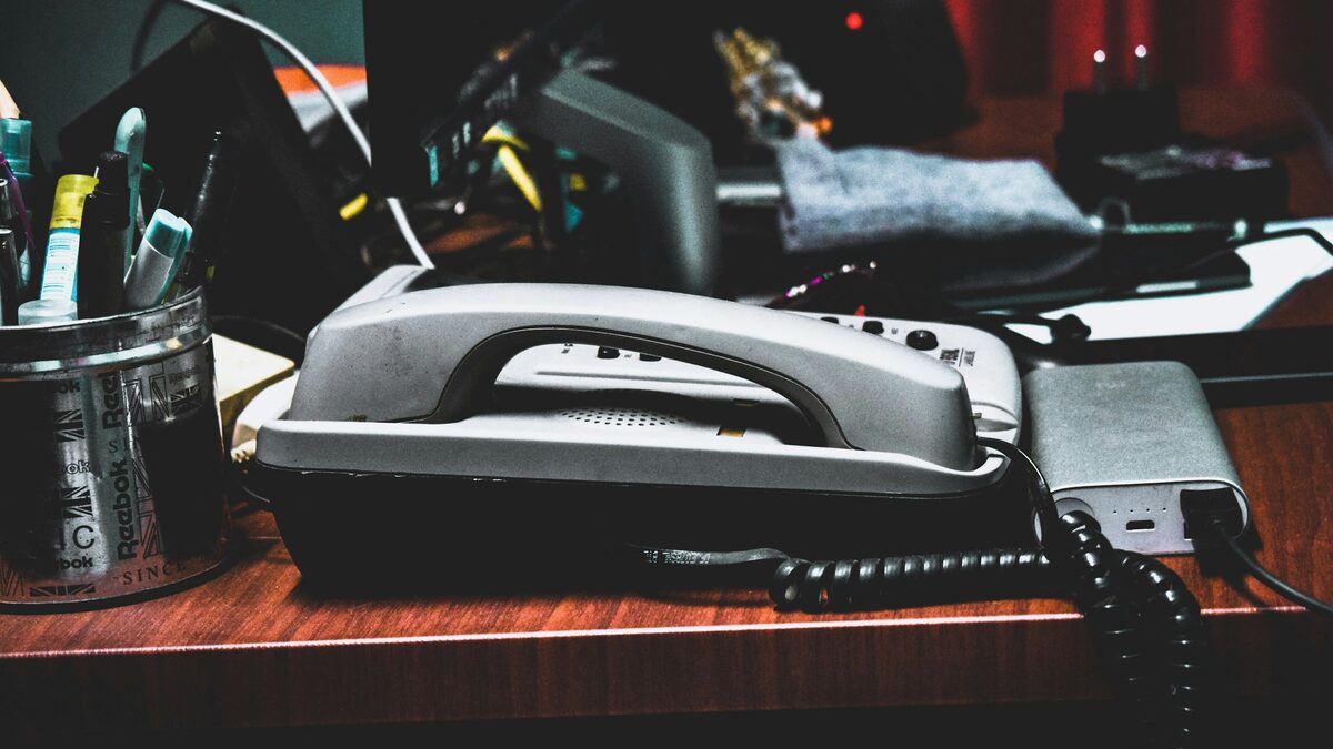 Graues Bürotelefon mit Spiralkabel auf einem Schreibtisch neben Stiften und Kabeln
