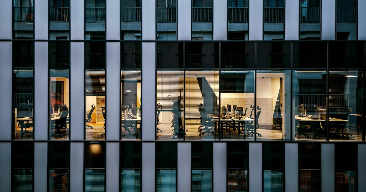 Fassade eines Bürogebäudes am Abend mit beleuchteten Büros hinter Glas