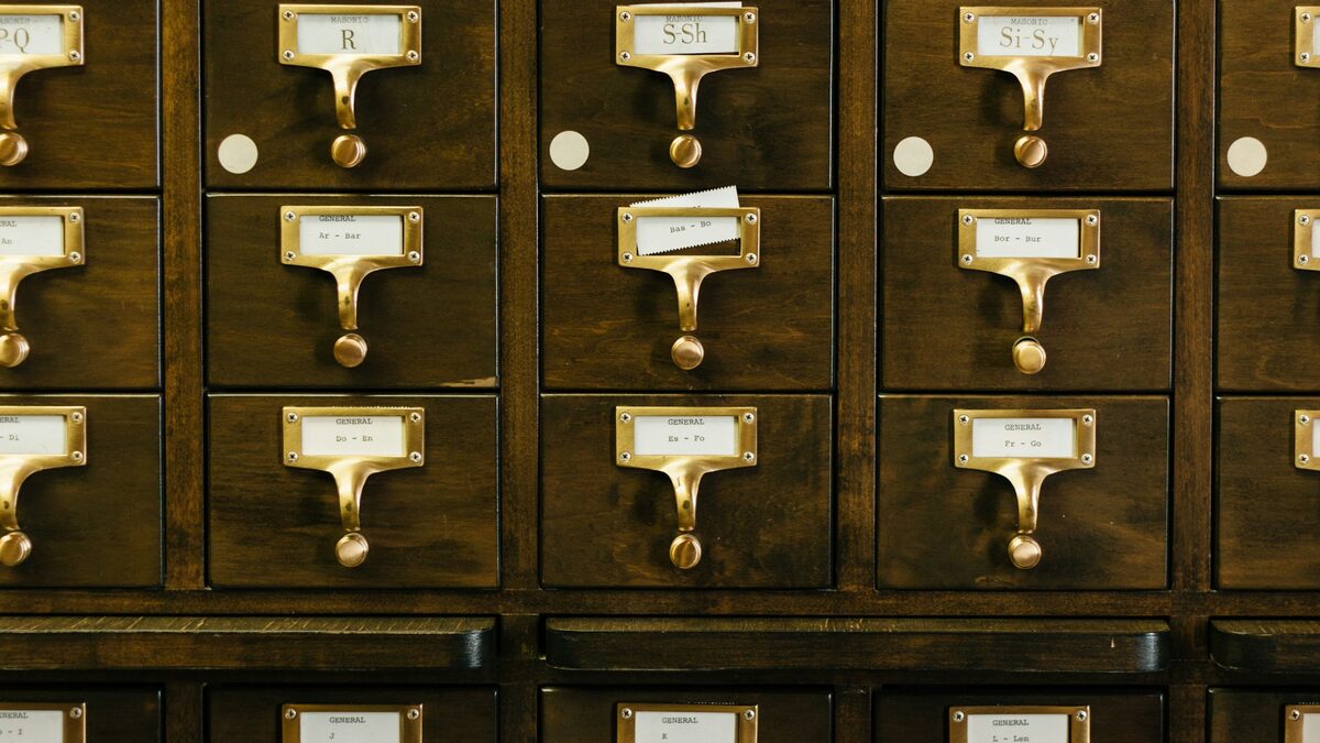 Wand aus hölzernen Karteikastenschubladen mit Messinggriffen und Beschriftungsschildern in einer Bibliothek