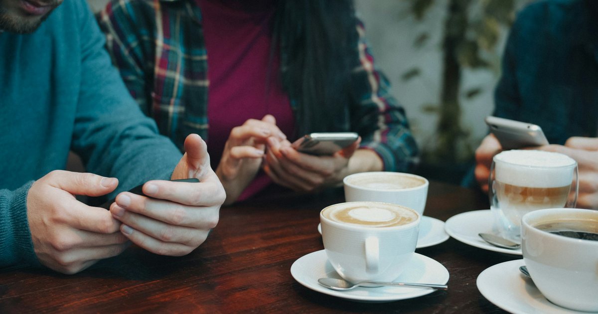 Drei Personen nutzen Smartphones an einem Holztisch mit Kaffeetassen
